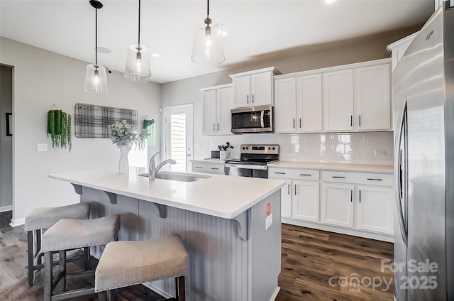 kitchen with appliances with stainless steel finishes, decorative light fixtures, white cabinetry, an island with sink, and sink