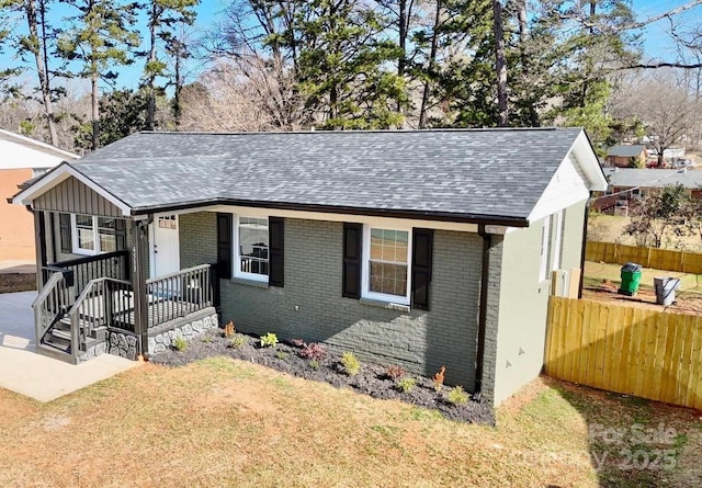 view of front facade with a front yard, fence, brick siding, and a shingled roof