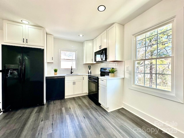 kitchen with dark wood-style floors, white cabinetry, black appliances, and a sink