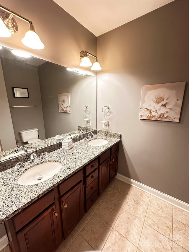 bathroom with double vanity, toilet, baseboards, and a sink