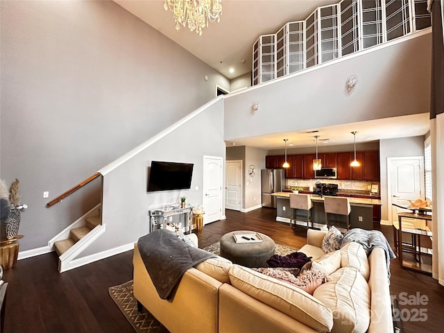 living room featuring baseboards, dark wood-type flooring, an inviting chandelier, stairs, and a high ceiling