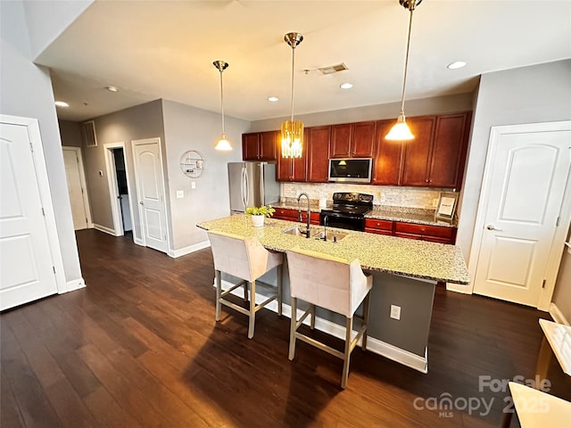 kitchen with a sink, appliances with stainless steel finishes, a breakfast bar, light stone countertops, and an island with sink