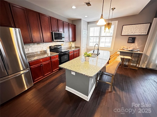 kitchen with dark brown cabinets, visible vents, a breakfast bar, appliances with stainless steel finishes, and an island with sink