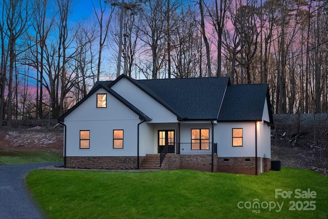 modern farmhouse style home with roof with shingles, brick siding, a porch, crawl space, and a front lawn