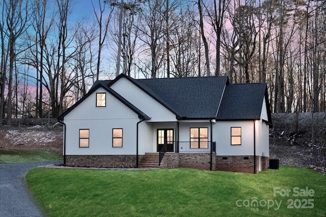 modern farmhouse featuring a lawn, roof with shingles, covered porch, crawl space, and brick siding