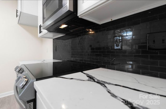 kitchen with white cabinetry, stainless steel appliances, light stone counters, and backsplash