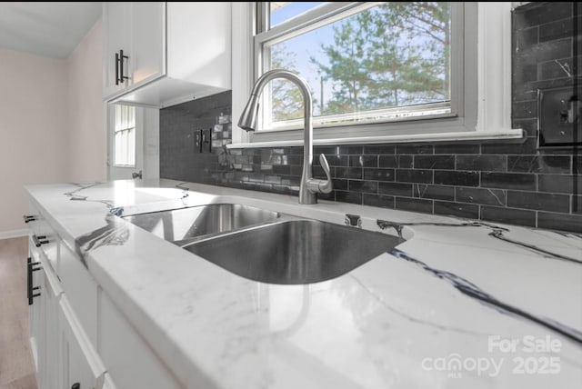 kitchen featuring sink, white cabinetry, wood-type flooring, light stone countertops, and decorative backsplash