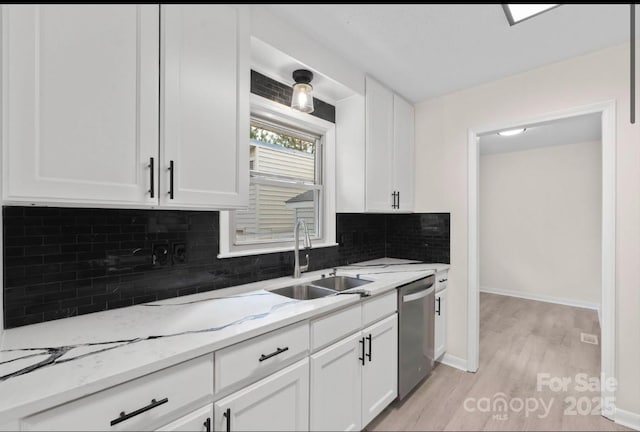 kitchen with sink, light stone counters, light hardwood / wood-style floors, white cabinets, and stainless steel dishwasher