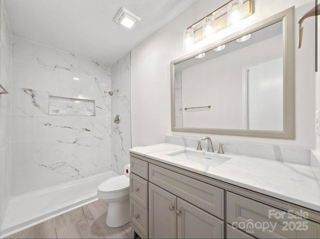 bathroom with vanity, tiled shower, and toilet