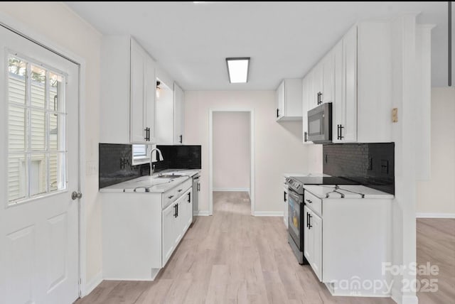 kitchen featuring sink, white cabinetry, light stone counters, light wood-type flooring, and appliances with stainless steel finishes