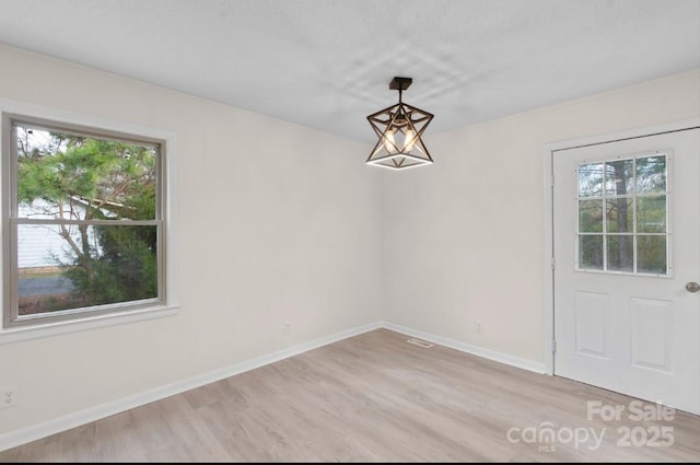 unfurnished dining area with a healthy amount of sunlight, a chandelier, and light hardwood / wood-style flooring