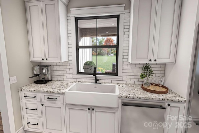 kitchen featuring light stone counters, white cabinetry, a sink, and backsplash