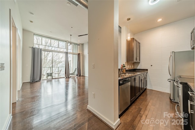 kitchen with appliances with stainless steel finishes, dark hardwood / wood-style floors, sink, hanging light fixtures, and expansive windows