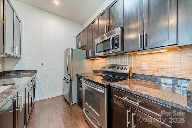 kitchen featuring dark brown cabinetry, dark wood-type flooring, dark stone counters, and appliances with stainless steel finishes