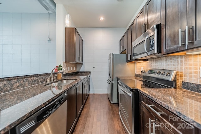 kitchen with appliances with stainless steel finishes, sink, hanging light fixtures, and dark stone counters