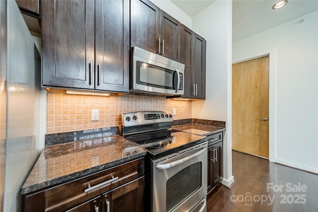 kitchen with dark brown cabinetry, appliances with stainless steel finishes, dark hardwood / wood-style flooring, dark stone counters, and backsplash