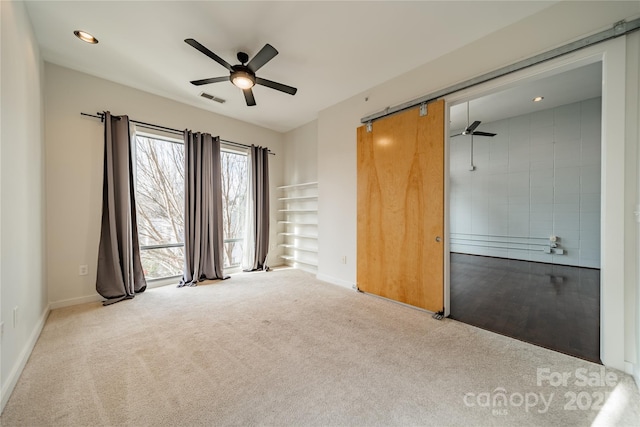 empty room featuring a barn door, light carpet, and ceiling fan