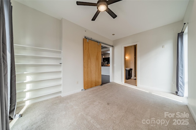 unfurnished bedroom with a barn door, light carpet, and ceiling fan