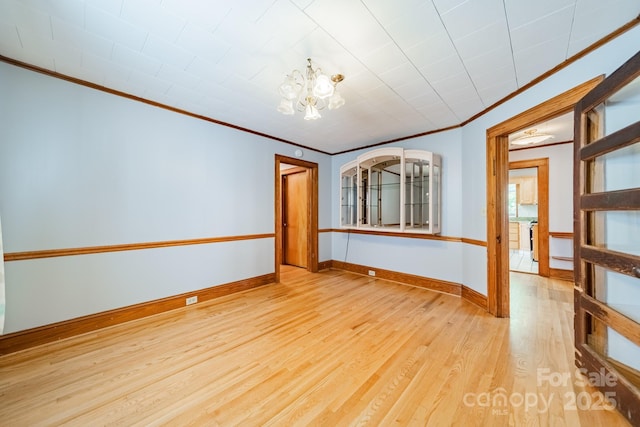 empty room featuring a notable chandelier, ornamental molding, and light hardwood / wood-style floors