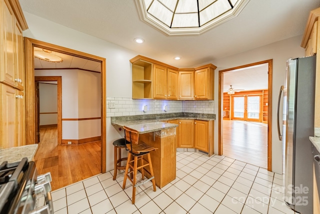 kitchen with appliances with stainless steel finishes, a kitchen bar, decorative backsplash, kitchen peninsula, and light stone countertops