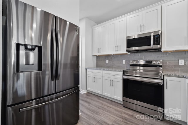 kitchen with appliances with stainless steel finishes, white cabinetry, tasteful backsplash, light stone countertops, and light wood-type flooring