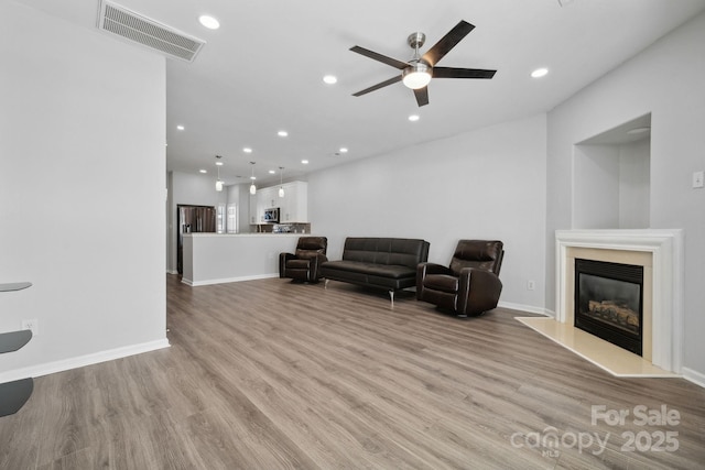 living room with a fireplace, light hardwood / wood-style flooring, and ceiling fan