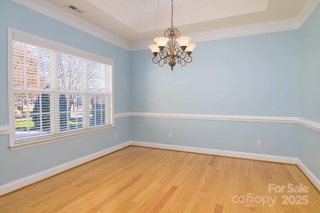 spare room featuring a raised ceiling, wood-type flooring, a notable chandelier, and crown molding