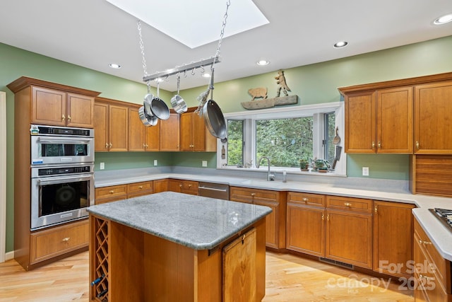 kitchen featuring sink, light hardwood / wood-style flooring, appliances with stainless steel finishes, a center island, and light stone counters