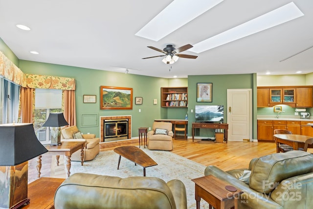 living room featuring rail lighting, sink, a skylight, ceiling fan, and light hardwood / wood-style floors