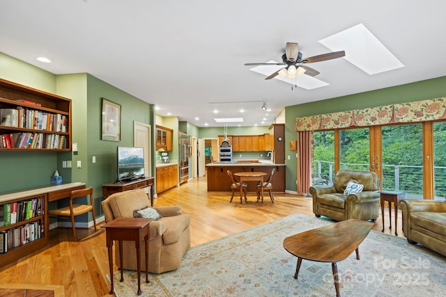 living room with a skylight, light hardwood / wood-style floors, and ceiling fan