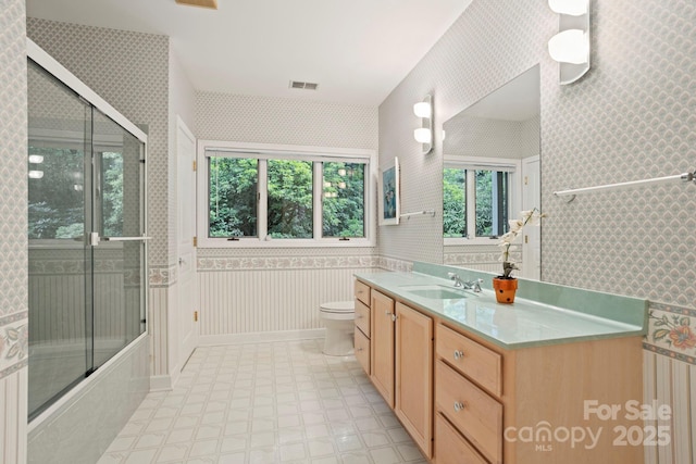 full bathroom with vanity, combined bath / shower with glass door, a healthy amount of sunlight, and toilet