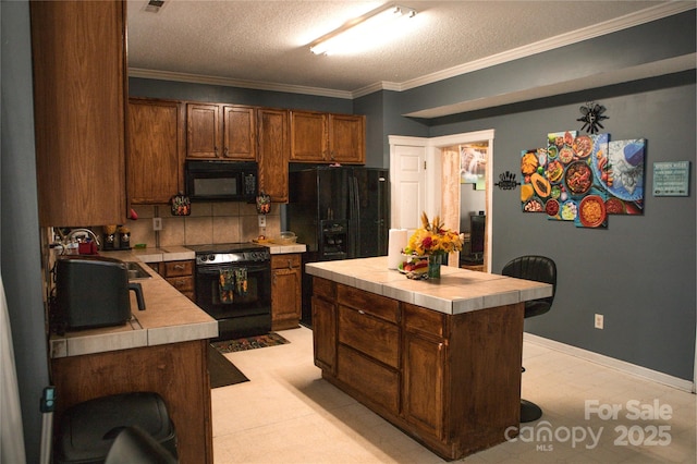 kitchen with ornamental molding, tile counters, a center island, and black appliances