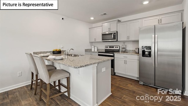 kitchen with sink, dark wood-type flooring, a breakfast bar area, appliances with stainless steel finishes, and light stone counters