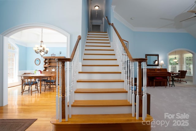 stairway featuring crown molding, ceiling fan with notable chandelier, a healthy amount of sunlight, and hardwood / wood-style flooring