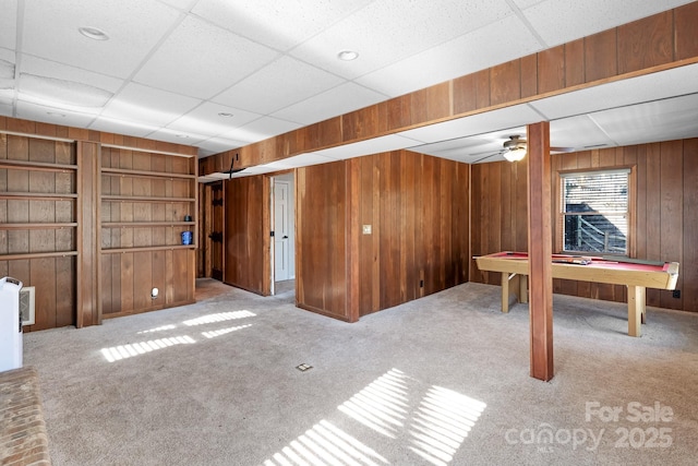 basement featuring light colored carpet, wooden walls, and built in shelves