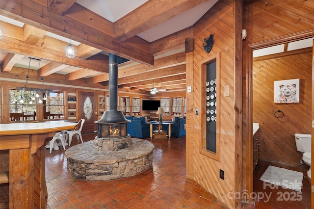 interior space with ceiling fan, wooden walls, beam ceiling, and a wood stove