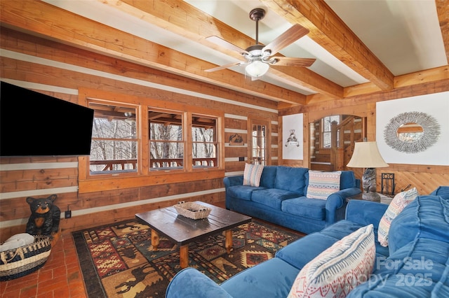 living room with beamed ceiling, ceiling fan, and wood walls