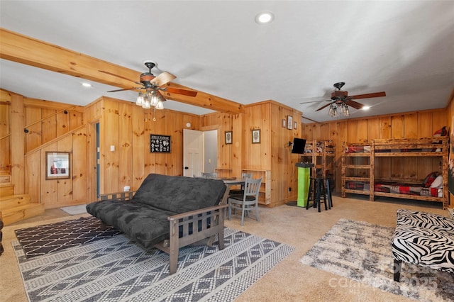 living room featuring ceiling fan, light colored carpet, beamed ceiling, and wood walls