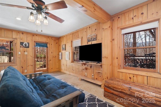 living room featuring ceiling fan, light colored carpet, beamed ceiling, and wood walls