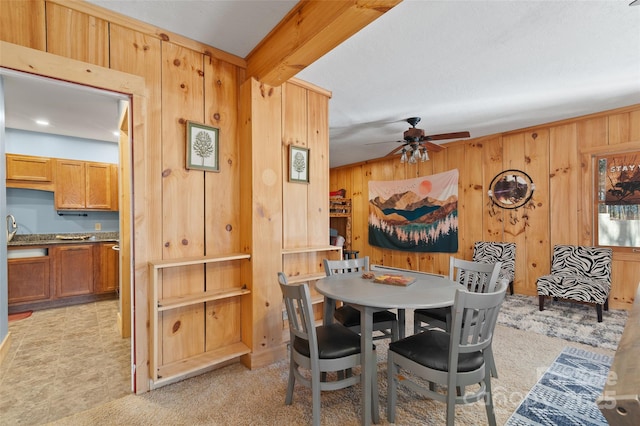 carpeted dining area featuring beam ceiling, ceiling fan, and wooden walls