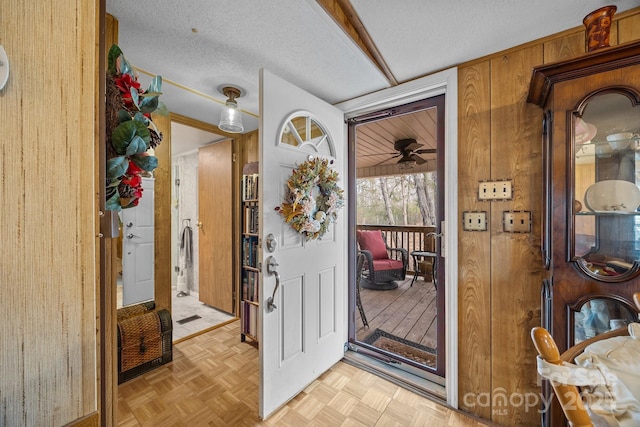 entryway featuring ceiling fan, wood walls, a textured ceiling, and light parquet floors