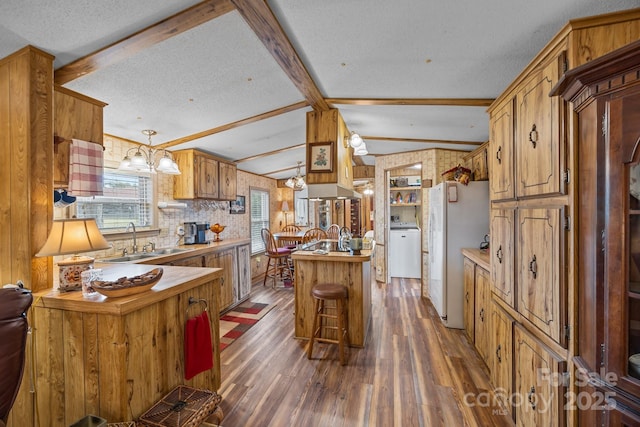 kitchen with dark hardwood / wood-style floors, lofted ceiling with beams, sink, white refrigerator, and hanging light fixtures