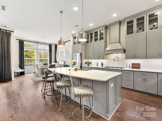 kitchen featuring premium range hood, tasteful backsplash, an island with sink, sink, and hanging light fixtures