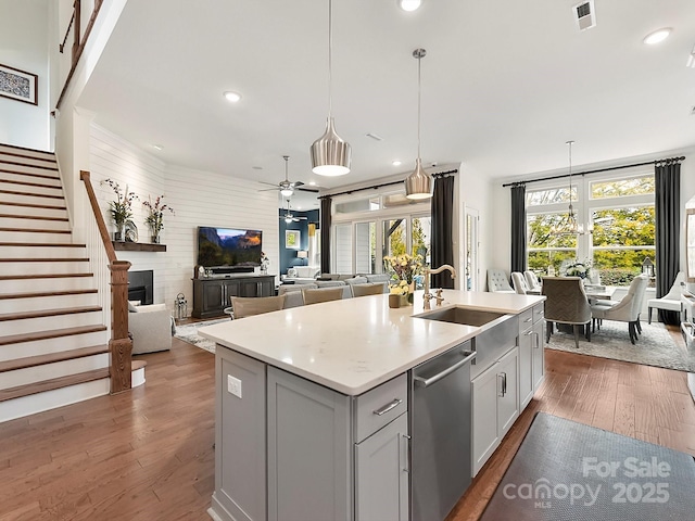 kitchen with pendant lighting, dishwasher, dark wood-type flooring, and a center island with sink