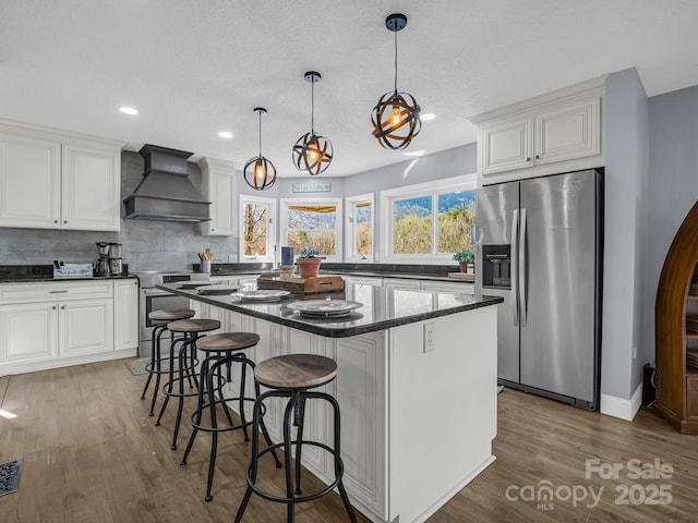 kitchen featuring premium range hood, a kitchen island, decorative light fixtures, white cabinets, and stainless steel appliances