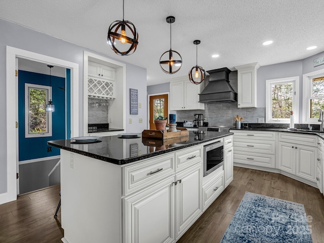 kitchen featuring stainless steel microwave, custom exhaust hood, white cabinets, and a kitchen island