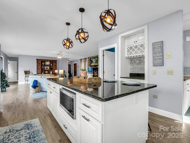 kitchen featuring pendant lighting, stainless steel microwave, white cabinetry, and a center island