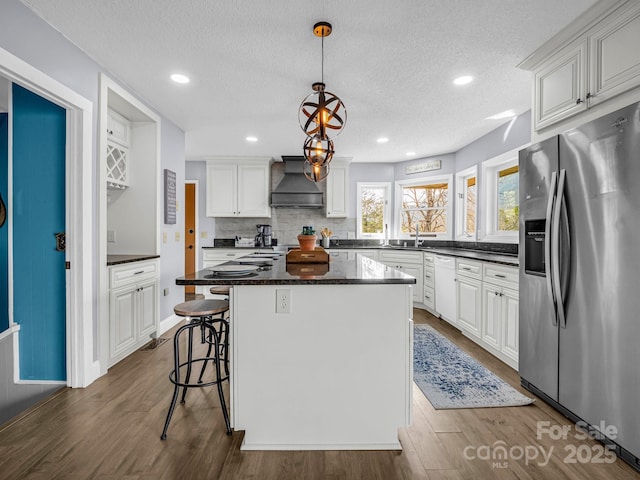 kitchen featuring custom exhaust hood, white cabinetry, a center island, stainless steel fridge, and pendant lighting