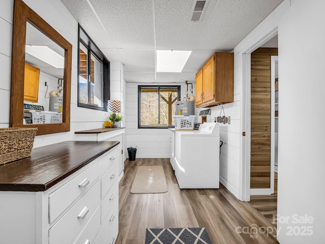 clothes washing area featuring washer and clothes dryer, electric water heater, cabinets, gas water heater, and light hardwood / wood-style floors