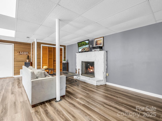 living room featuring wood-type flooring, a stone fireplace, a paneled ceiling, and wood walls